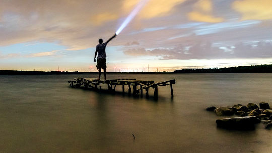 Blessing for Spiritual Seekers and for People Suffering from Depression man standing on a dock shining a flashlight into the sky