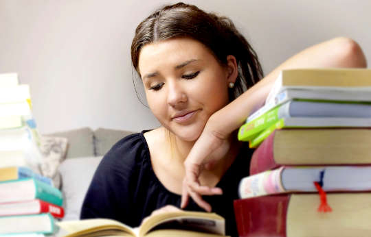 8 Steps to Take You from Turmoil to Tranquility a young woman peacefully reading a book with her arm resting a whole stack of books