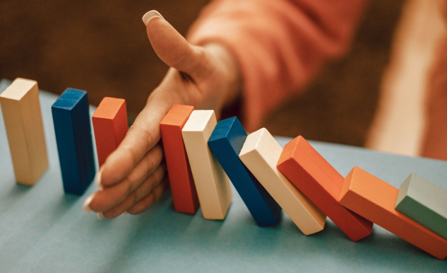 Why Are Cause and Effect Better Than Luck? Dominos starting to tumble with a hand stopping them. Image by Oleksandr Pidvalnyi from Pixabay.